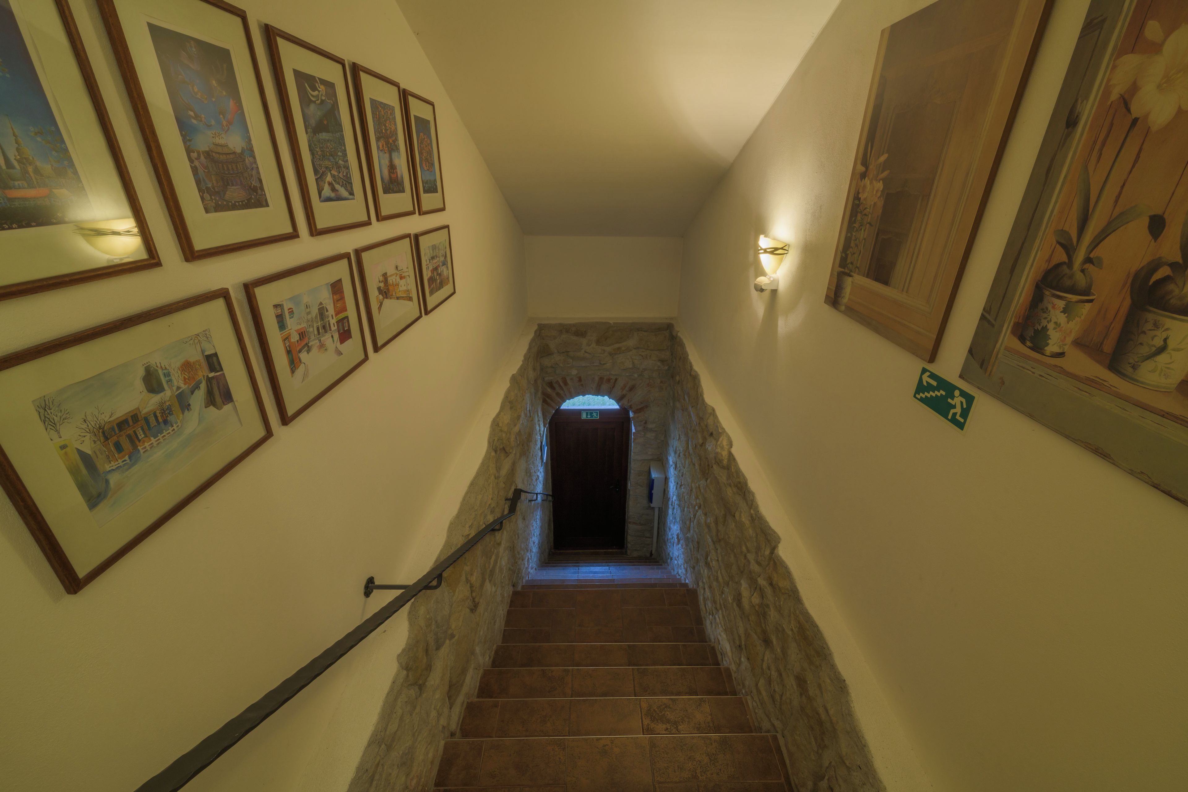 Un escalier avec des murs en pierre et des tableaux encadrés sur le côté gauche.