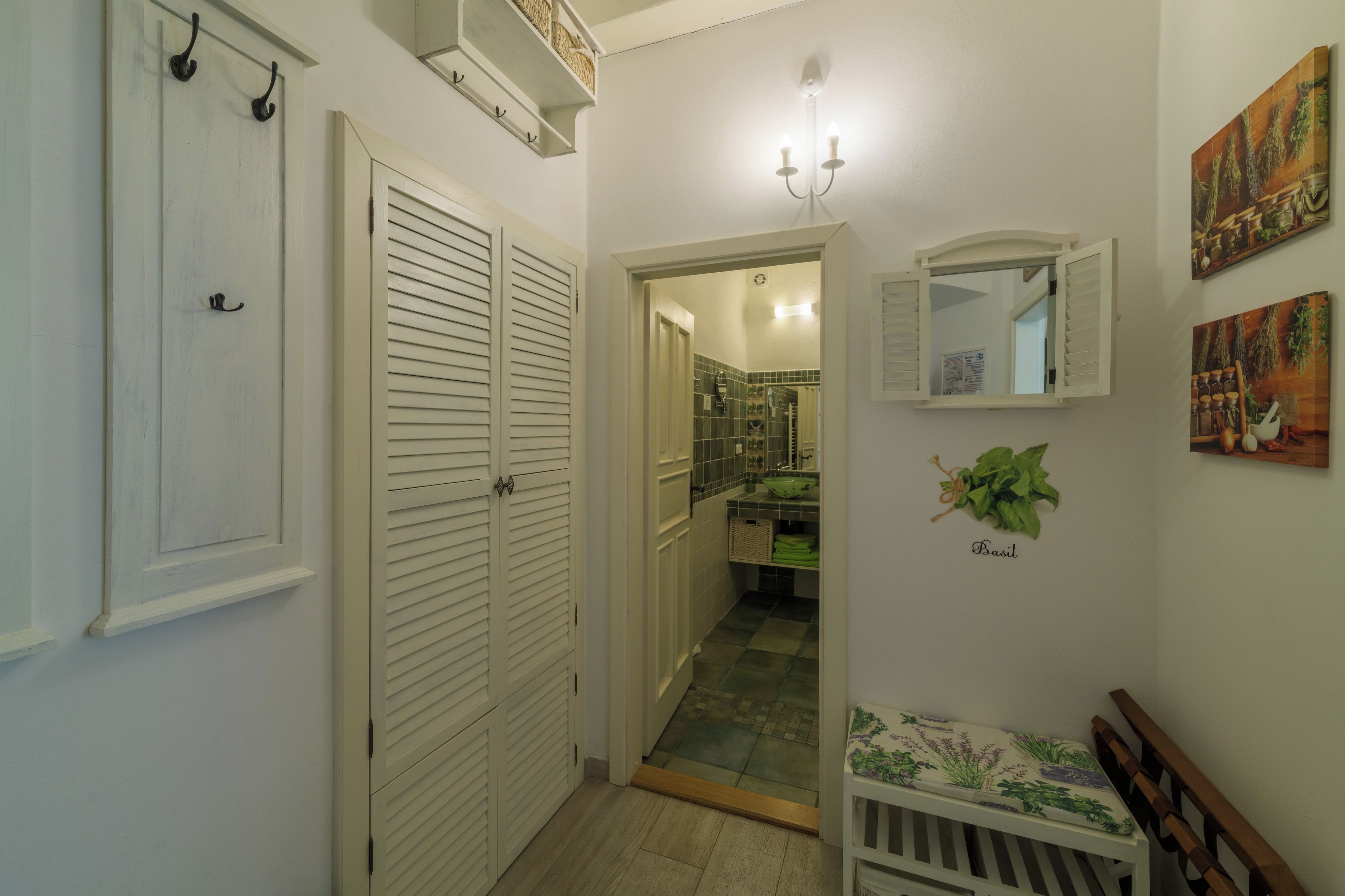 Un pasillo con una puerta blanca, un espejo y una cama pequeña con una planta verde.
