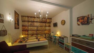 A bedroom with a bed, a desk, a chair, a dresser, and a wall with vintage-style wallpaper.
