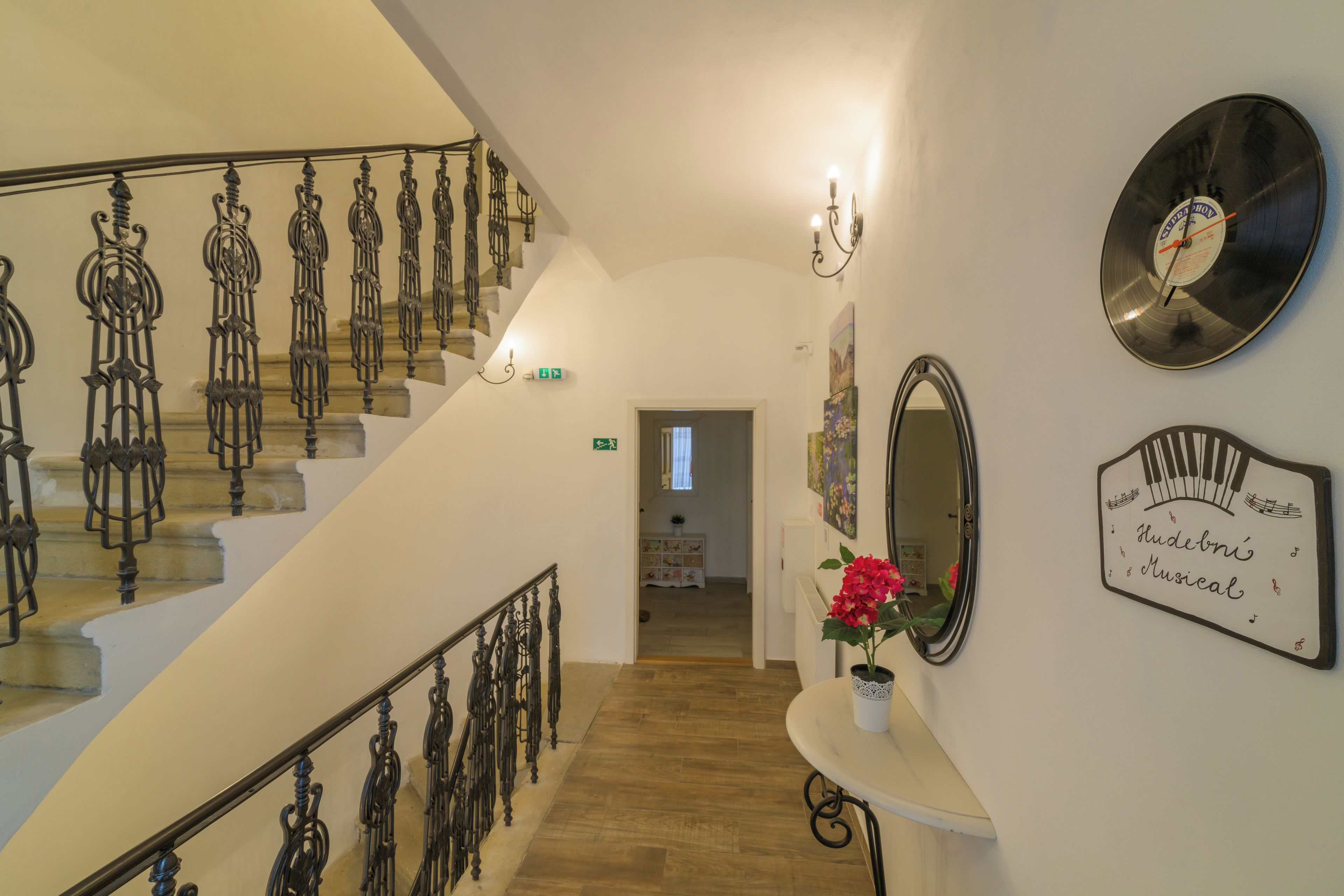 Una escalera con barandillas de metal decoradas, un reloj de pared, un espejo y un letrero con notas musicales.