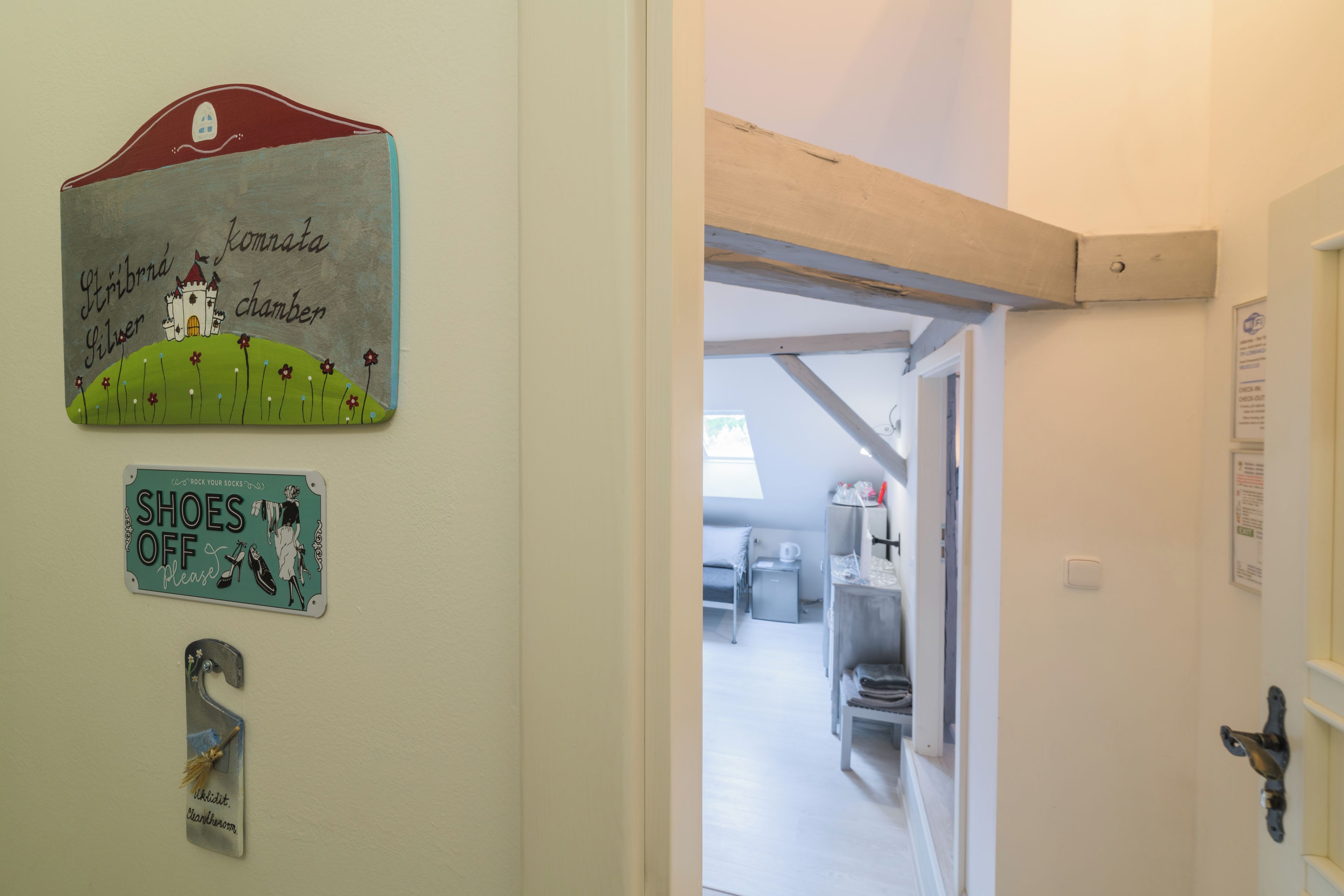Un pasillo con una puerta que da a una habitación, una pared con una ilustración de un castillo y un cartel que dice 'SHOES OFF Please'.