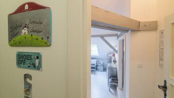 Un pasillo con una puerta que da a una habitación, una pared con una ilustración de un castillo y un cartel que dice 'SHOES OFF Please'.