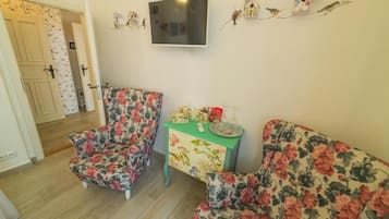 A room with two floral-patterned sofas, a small table with a decorative item, and a wall-mounted TV.