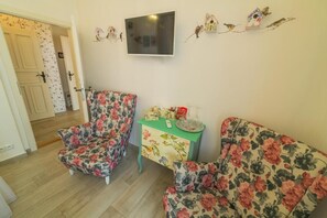 A room with two floral-patterned sofas, a small table with a decorative item, and a wall-mounted TV. - Penzion U Zámku Mělník (Mělník)