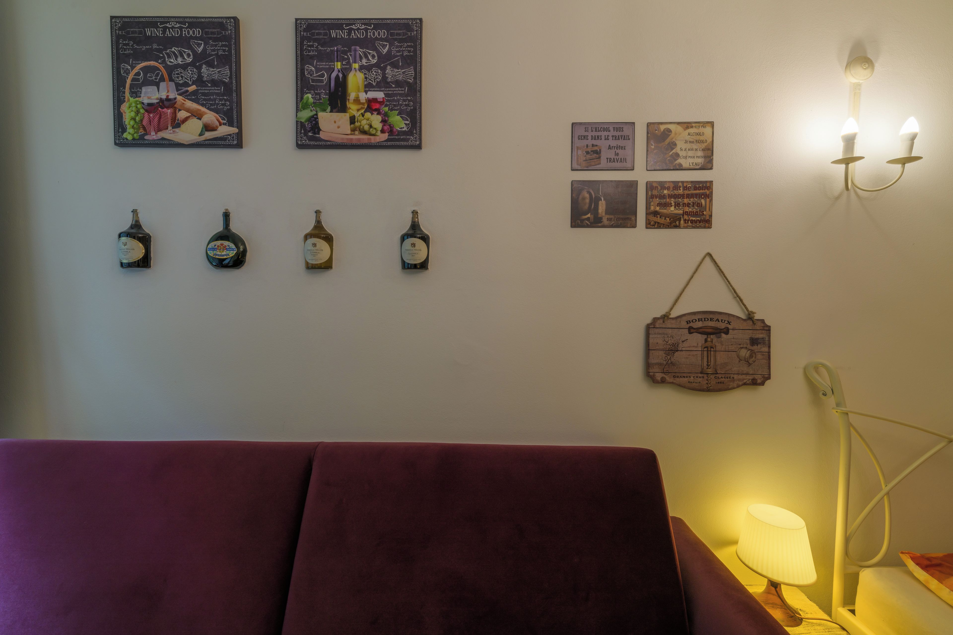 A room with a red sofa, wall-mounted wine bottles, and various posters.