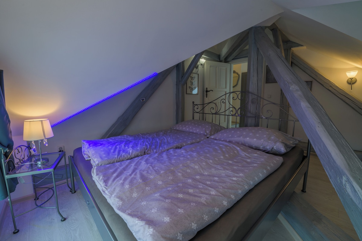 Un dormitorio con una cama, una mesita de noche, una lámpara y una escalera.