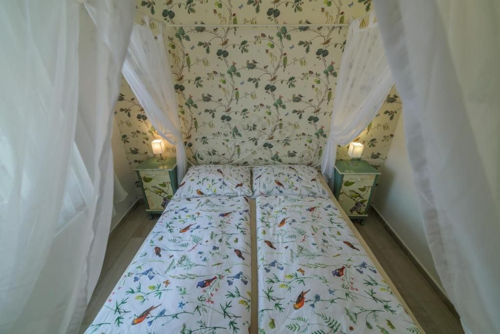Uma cama com colcha florida, duas mesas de cabeceira com abajures e um dossel.