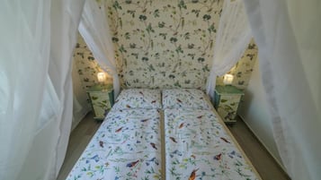 Uma cama com colcha florida, duas mesas de cabeceira com abajures e um dossel.