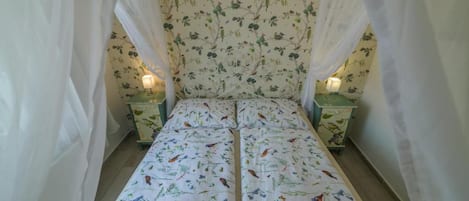 Una cama con una colcha estampada con flores, dos mesitas de noche con lámparas y un dosel.