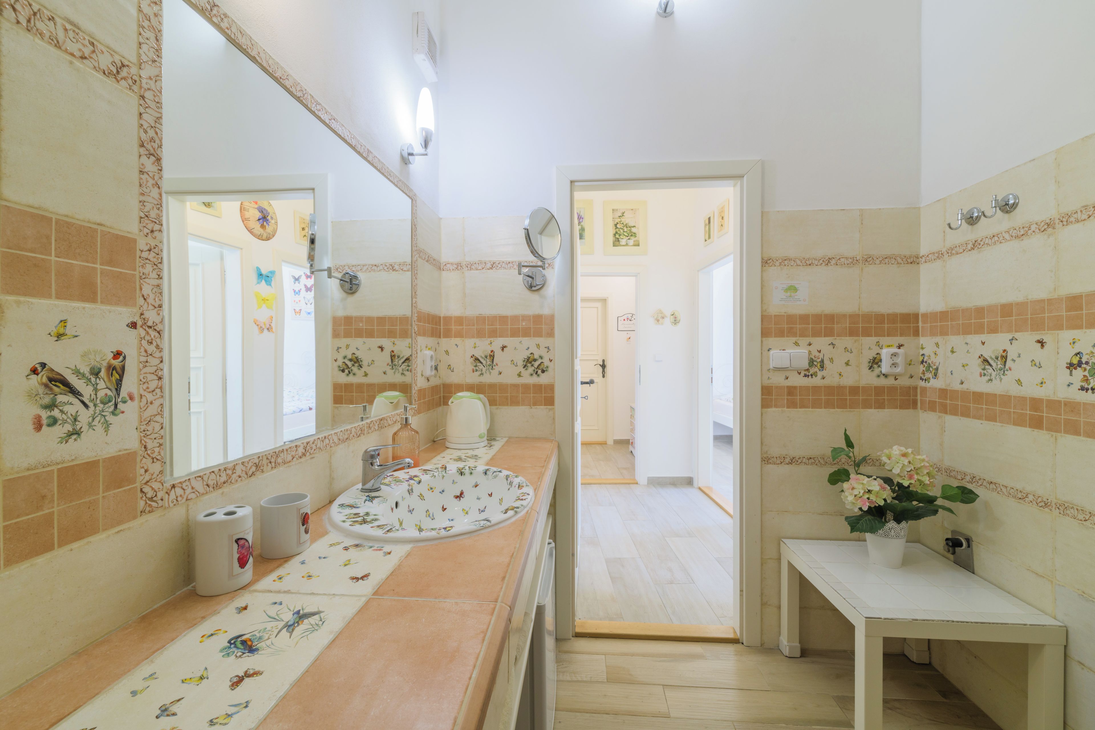 A bathroom with a floral tile backsplash, a sink with a floral pattern, a mirror, and a door leading to another room.