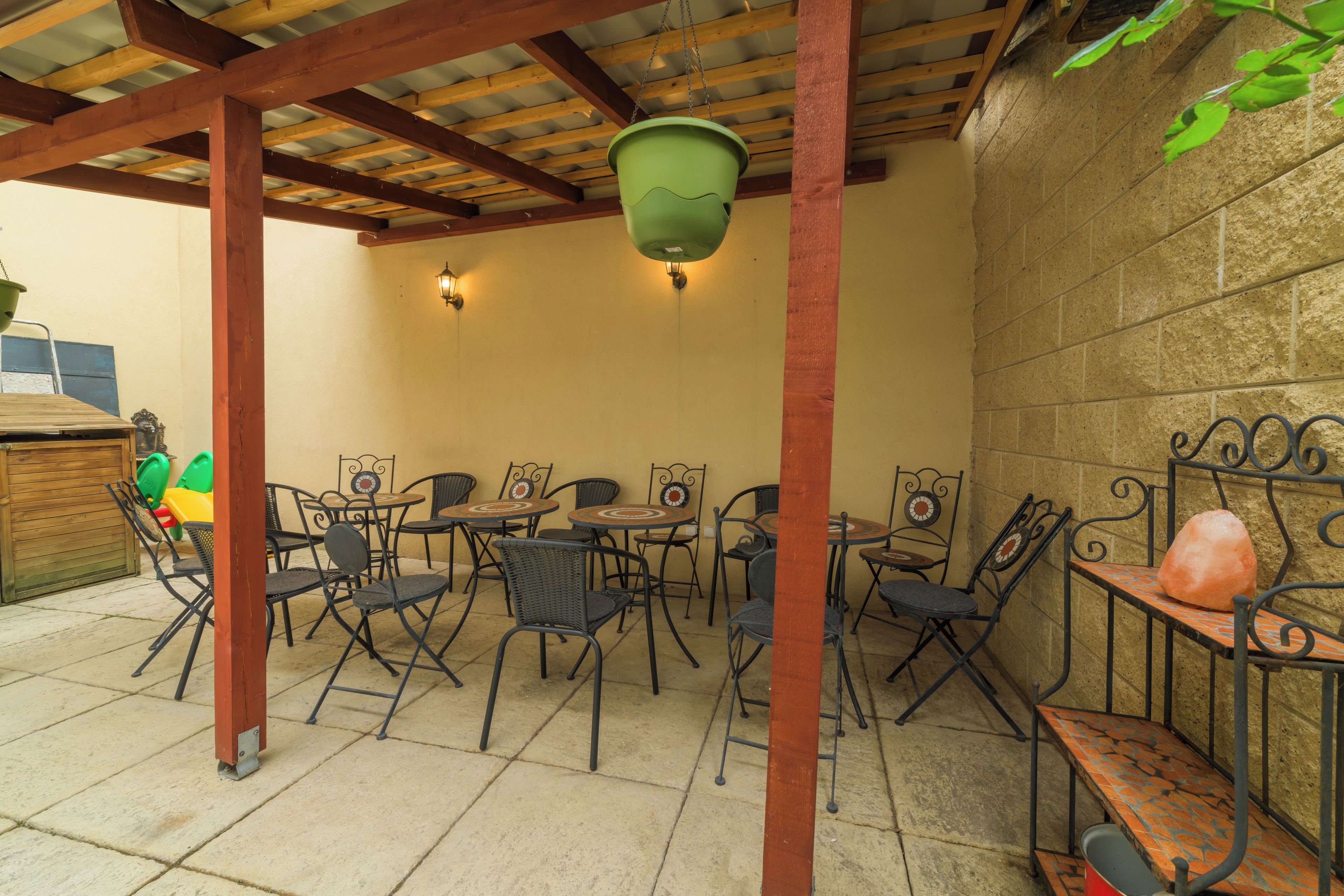 An outdoor patio with metal tables and chairs, a hanging light fixture, and a stone wall.
