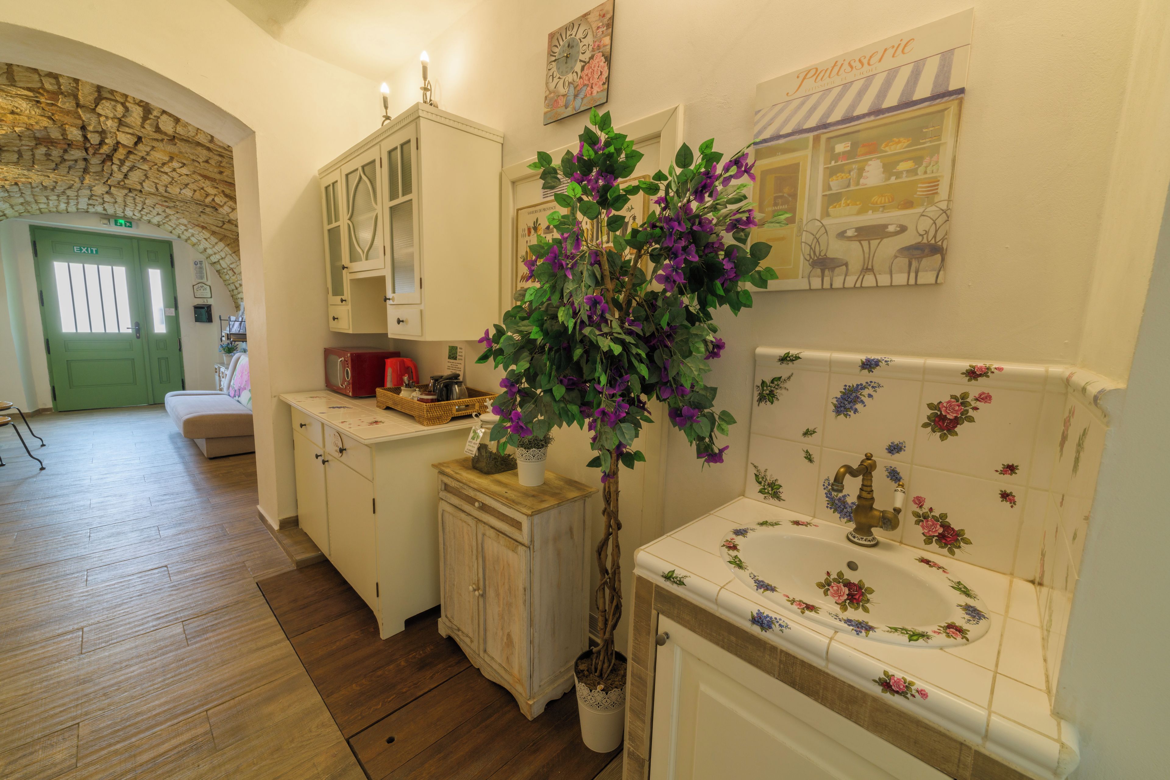 Una cocina con suelo de madera, una puerta verde, un armario blanco y una planta en maceta.