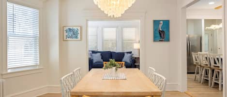 Une salle à manger avec une table en bois, des chaises blanches, un canapé bleu et un lustre.