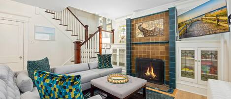 A living room with a fireplace, a staircase, and a painting of a beach scene.