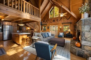A spacious cabin interior with a high ceiling, a stone fireplace, a kitchen area, and a cozy seating area. - Gatlinburg Mountain Cabin Views Hot Tub Game Room Sleeps 9 (Gatlinburg)