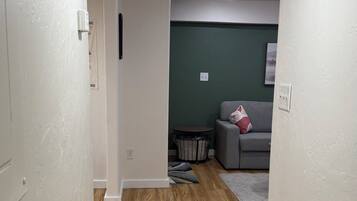 A hallway with wooden flooring, a grey sofa, and a green wall in the background.