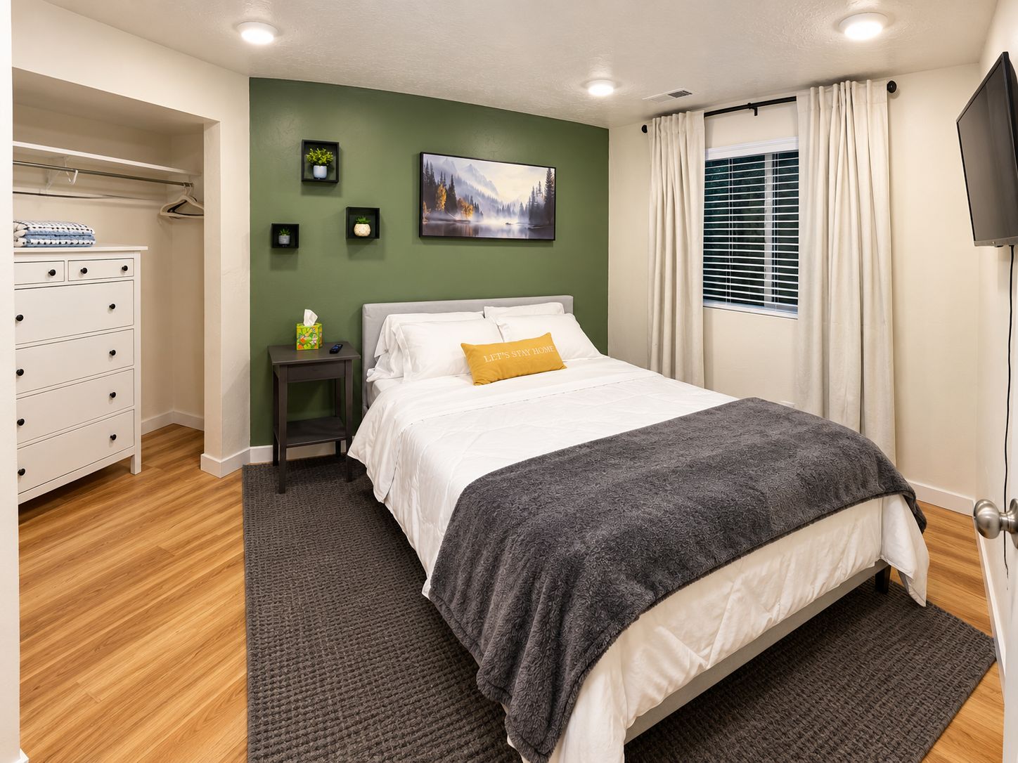 A bedroom with a bed, a nightstand, a dresser, a painting, and a window with curtains.