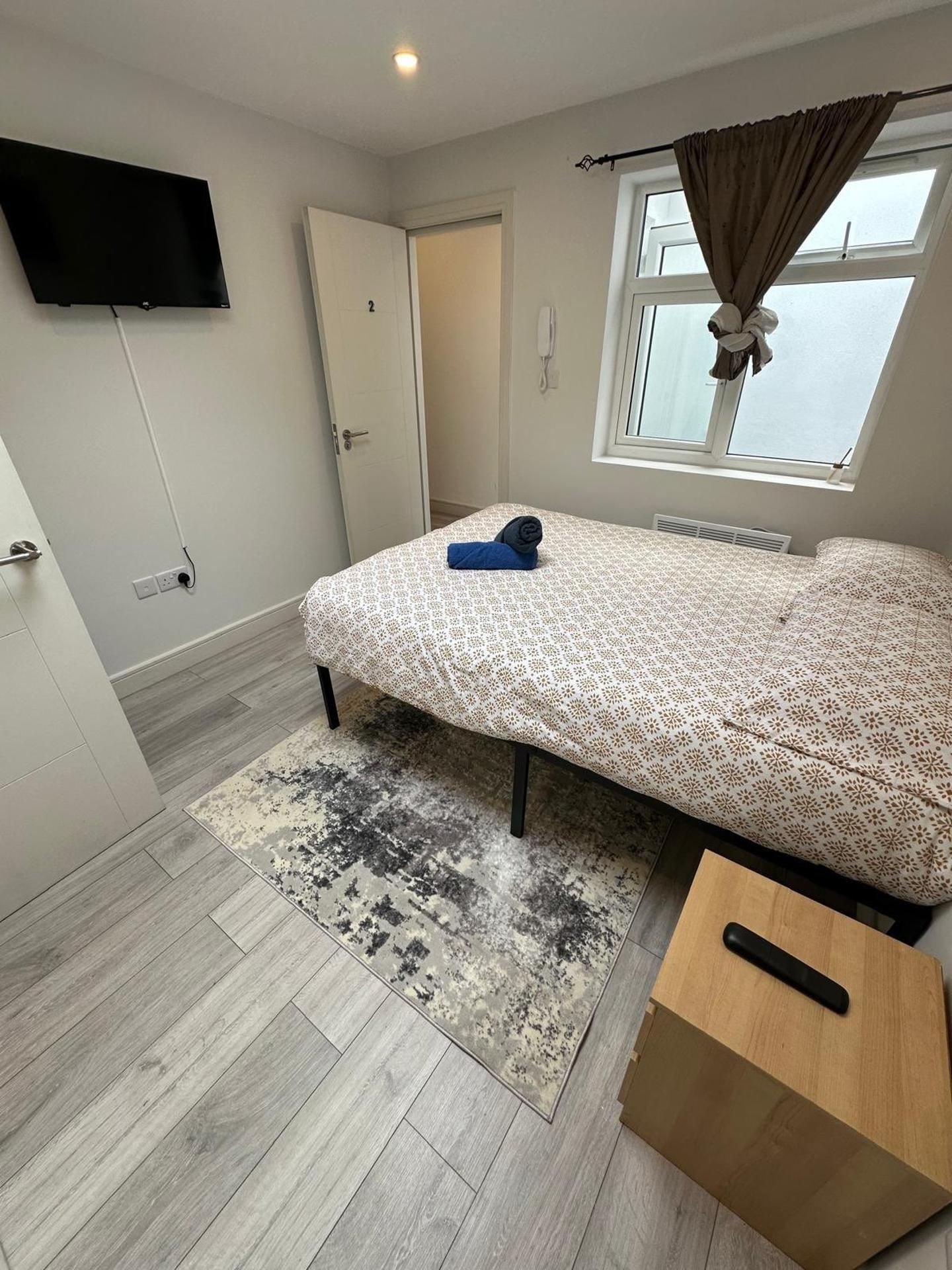A bedroom with a bed, a television mounted on the wall, a window with curtains, and a door.
