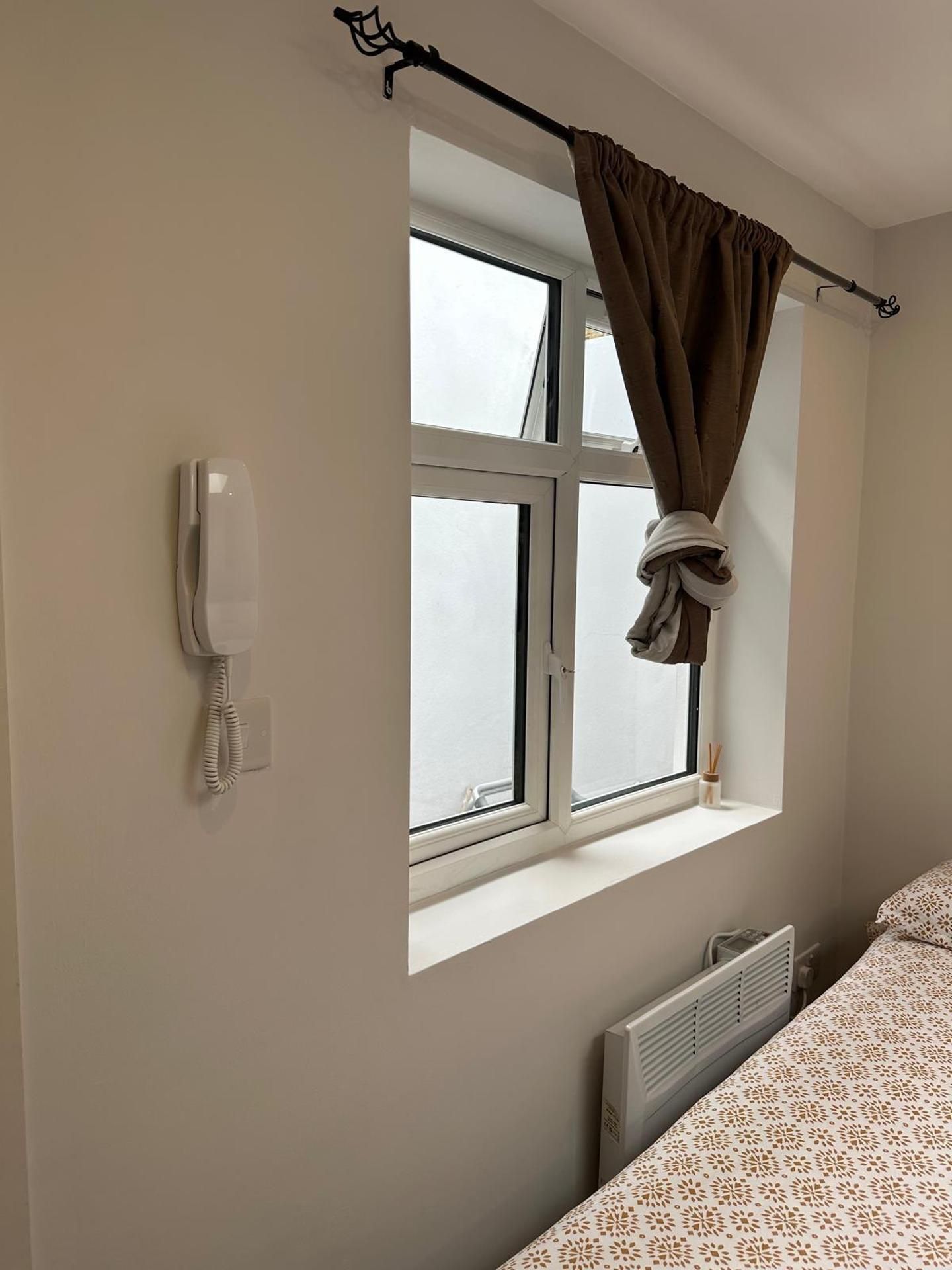 A room with a bed, a window with curtains, a radiator, and a telephone.