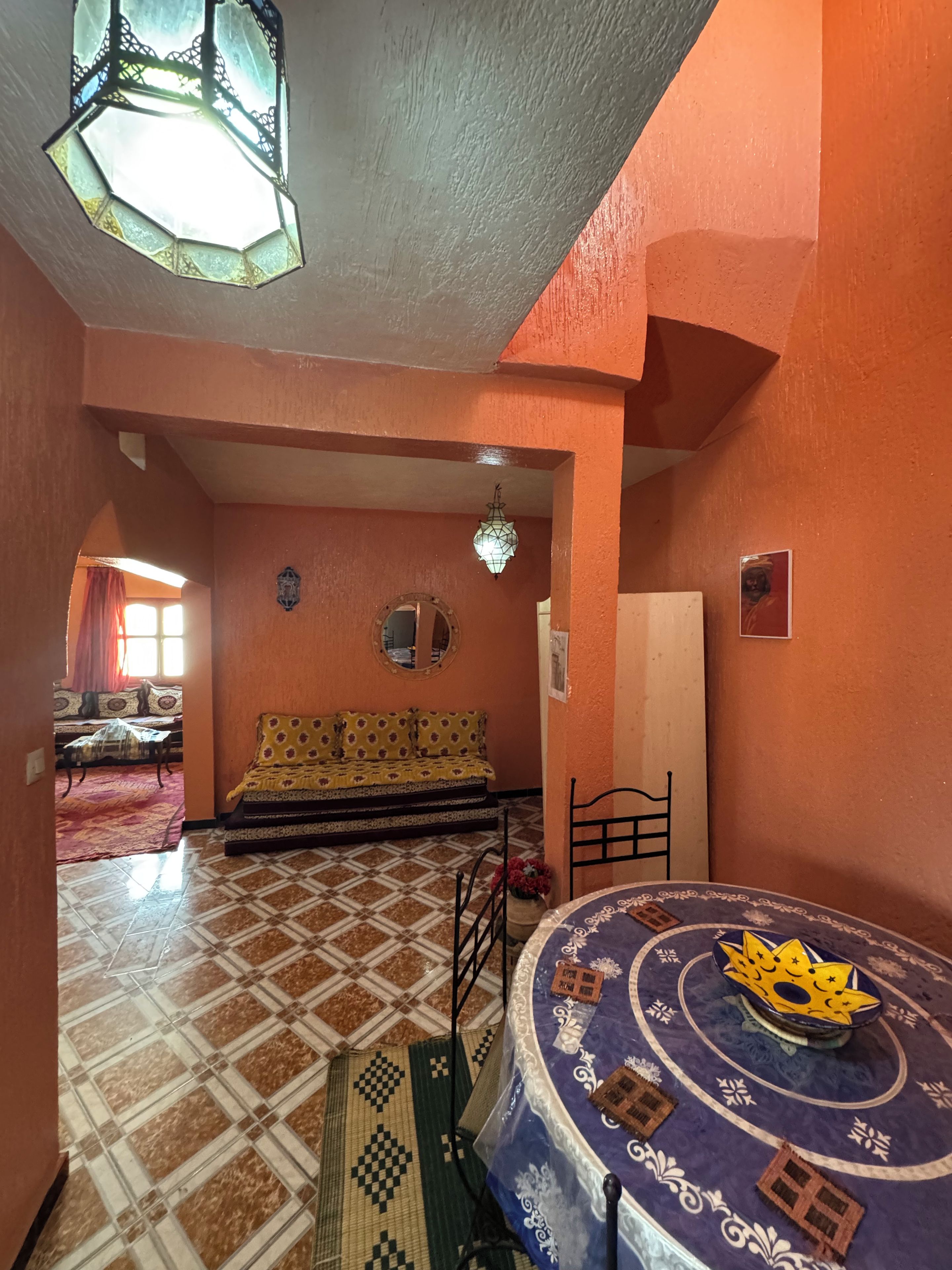 Une pièce avec un sol à motifs, un lit recouvert d’une couvre-lit à motifs, un miroir fixé au mur et une table décorative avec une nappe à motifs.