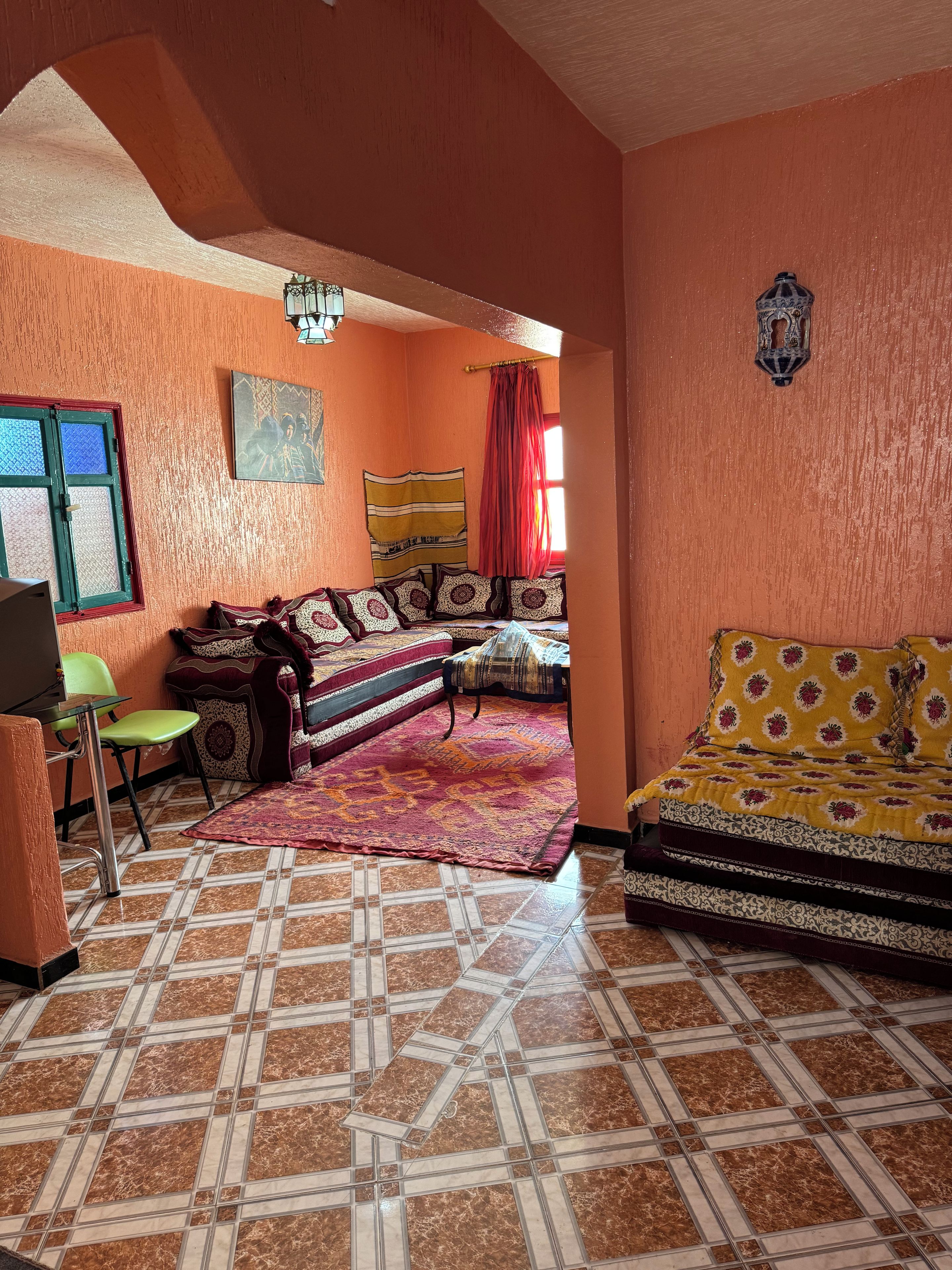 A room with a sofa, a bed, a patterned rug, and a window with curtains.