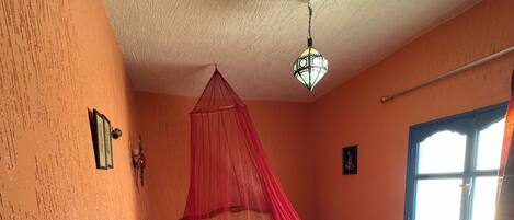 A room with a bed under a red canopy, a green chair, a window, and a patterned rug.