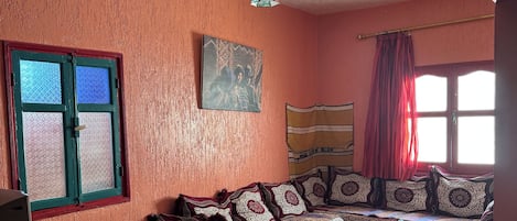 A room with a sofa set, a chair, a table, a patterned rug, a painting, and a window with curtains.