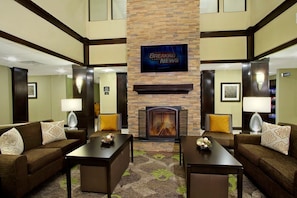 A hotel lobby with a fireplace, two sofas, a coffee table, and a television displaying 'Breaking News'.