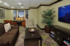 A living room with a brown sofa, a beige armchair, a coffee table, a TV, and a bookshelf.