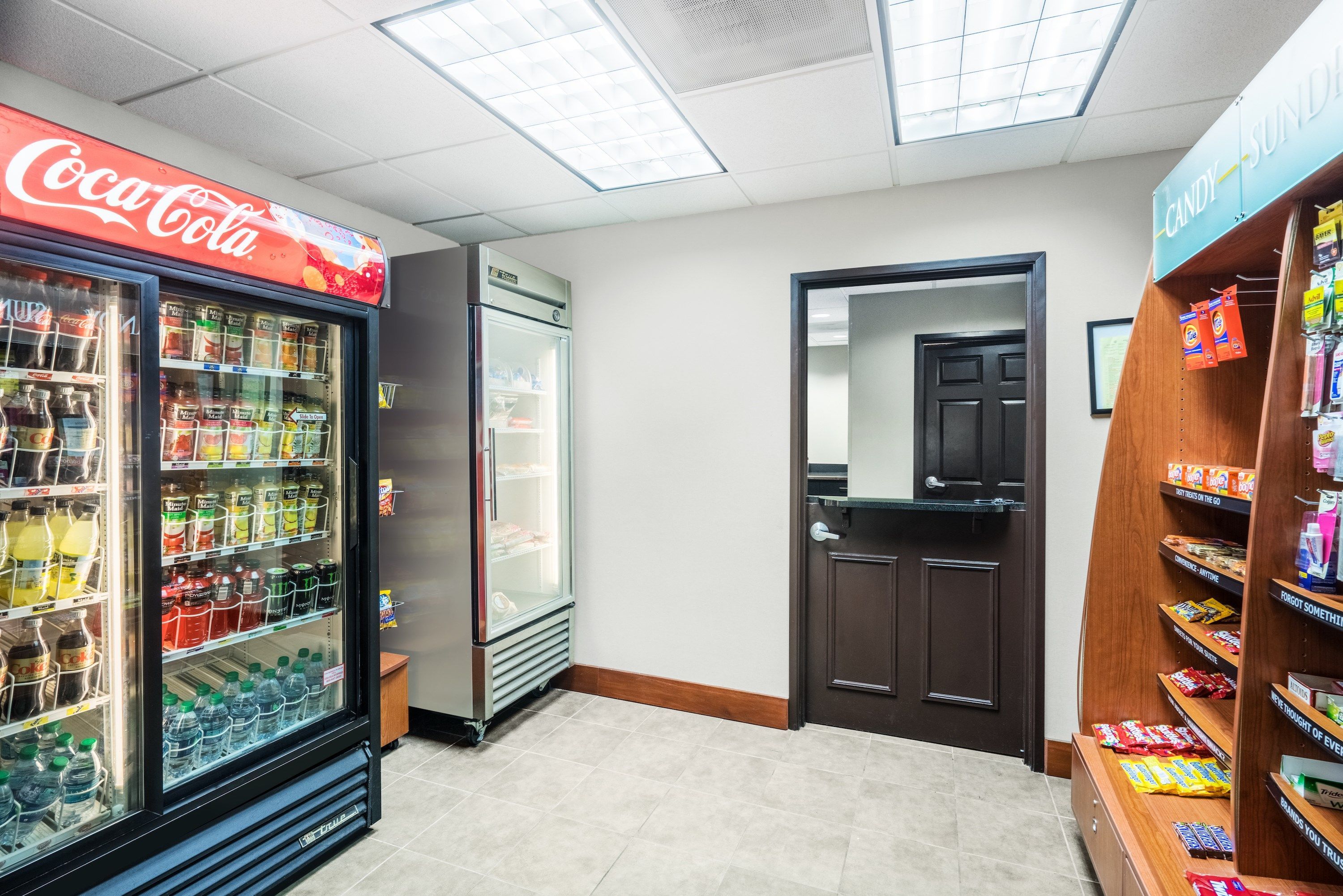 A Coca-Cola refrigerator, a freezer, and a candy shelf in a store.