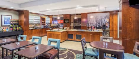 A hotel lobby with a breakfast bar, seating area, and a TV mounted on the wall.