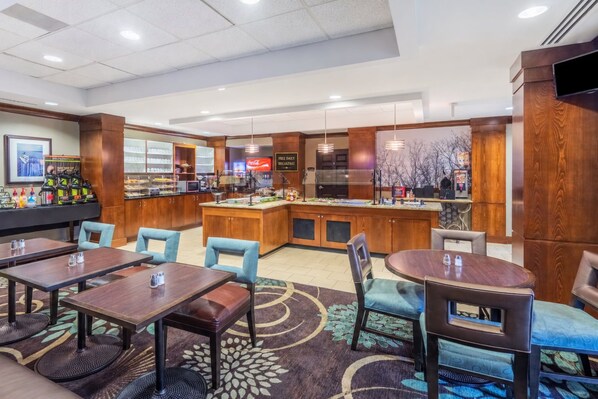 A hotel lobby with a breakfast bar, seating area, and a TV mounted on the wall.