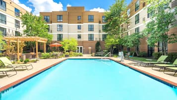 A swimming pool with lounge chairs and a pergola, surrounded by multi-story buildings with balconies.