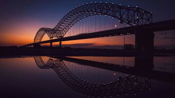 A bridge with a distinctive arch design, spanning over a body of water, with its reflection visible in the water below.