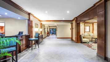 A spacious lobby with a reception desk, seating area, and a view into a room.