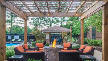 Une terrasse extérieure avec des meubles en osier, un foyer en pierre et une piscine en arrière-plan.