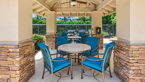 An outdoor patio with a round table and blue chairs, surrounded by stone walls and a ceiling fan. - Studio Suite w/ Roll-in Shower | Free Breakfast! (Memphis)
