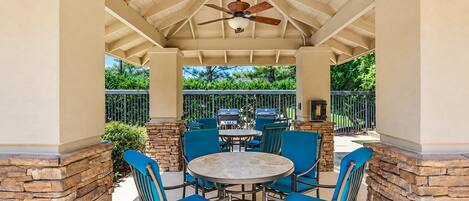An outdoor patio with a round table and blue chairs, surrounded by stone walls and a ceiling fan.