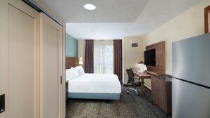 A hotel room with a bed, desk, chair, television, and a refrigerator. - Studio Suite w/ Roll-in Shower | Free Breakfast! (Memphis)
