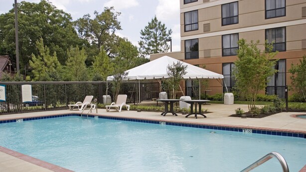 A swimming pool with lounge chairs and a table under a canopy, surrounded by a fence and trees. - Studio Suite w/ Roll-in Shower | Free Breakfast! (Memphis)