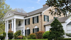 A large, two-story house with a stone facade, green shutters, and a well-maintained lawn. - Studio Suite w/ Roll-in Shower | Free Breakfast! (Memphis)