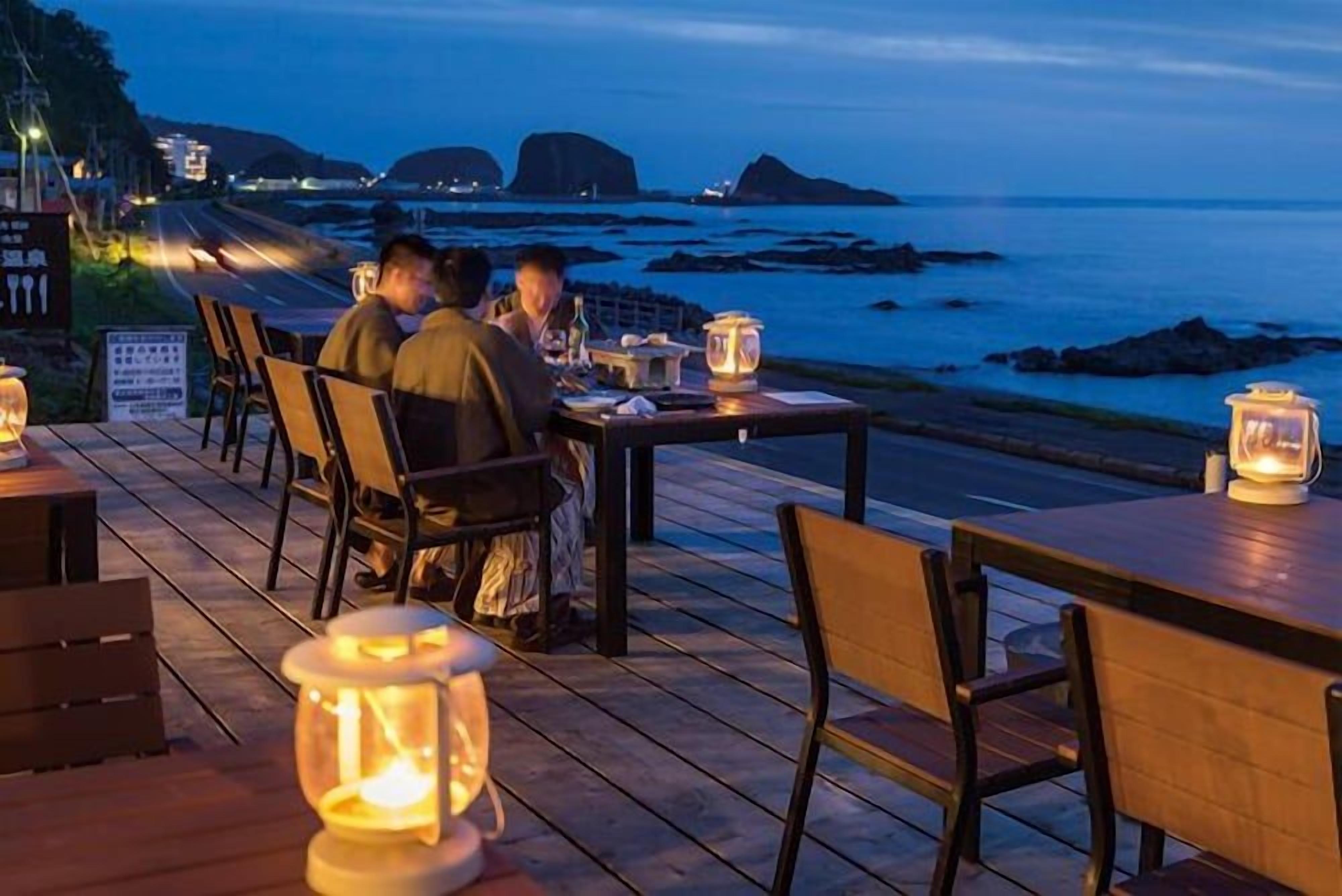 Un espacio exterior para comer con mesas y sillas, vista al océano y una terraza de madera.