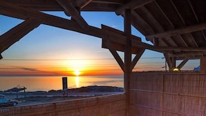 Estructura de madera con vista al atardecer sobre el agua, un jacuzzi y una zona con piedras.