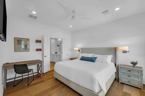 A hotel room with a bed, bedside table, desk, chair, and a ceiling fan. - Beachy Vibes - Gulf Views • Beach Access • Sleeps 12 (Bolivar Peninsula)