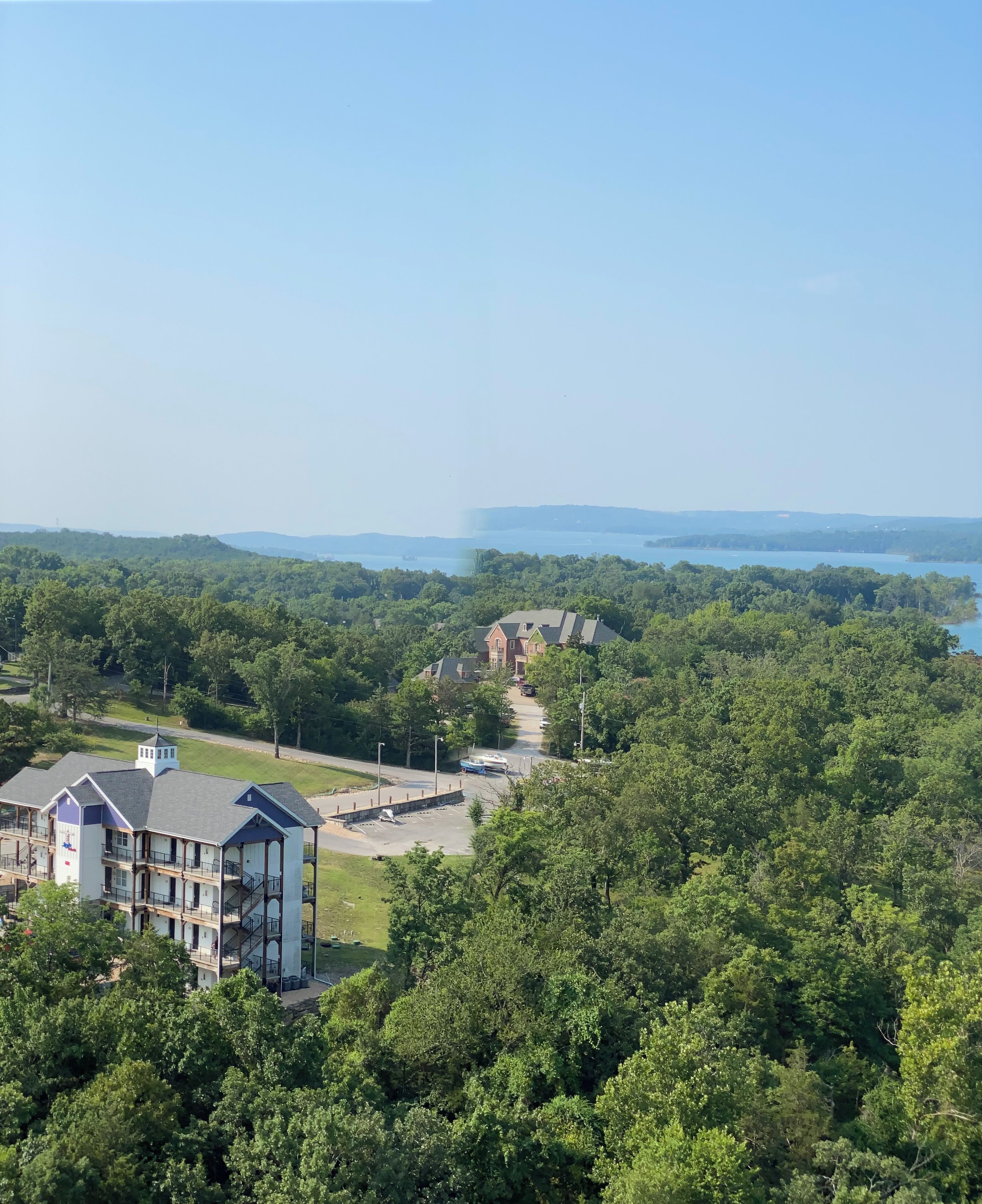 Un immeuble à plusieurs étages doté d’un parking et offrant une vue sur un lac et une zone boisée.