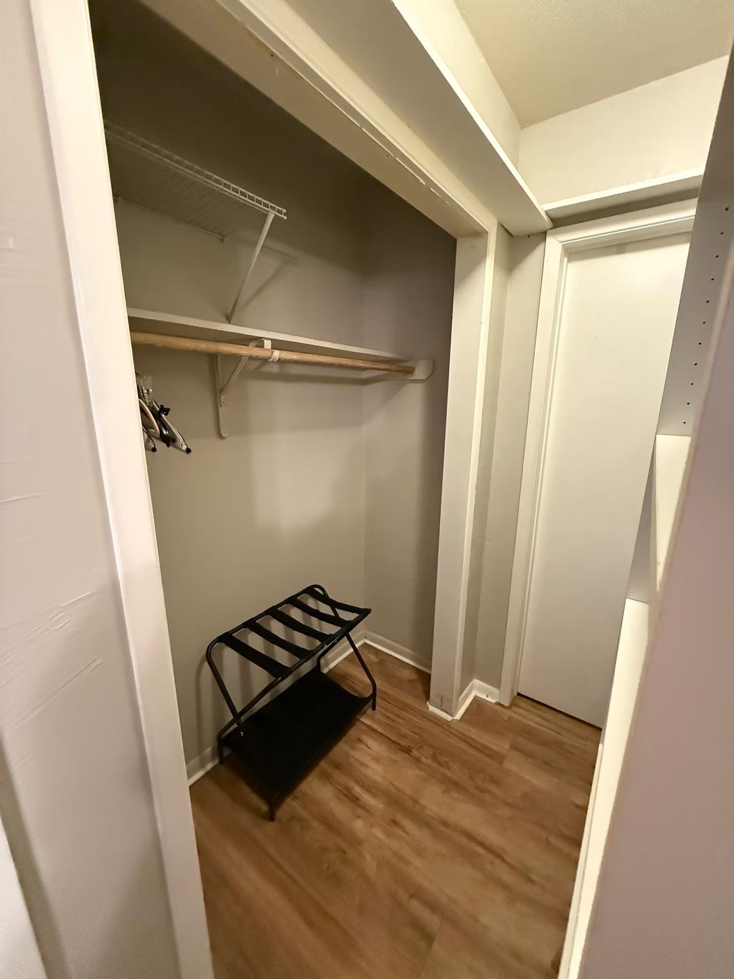 Um closet amplo com piso de madeira, uma estante de metal preta e uma porta branca.
