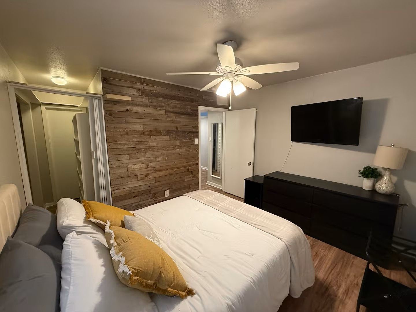 Ein Schlafzimmer mit einem Bett, einem Deckenventilator, einem Fernseher und einem Schminktisch.