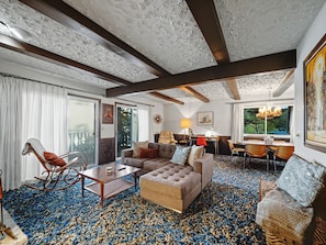 A spacious living room with a large sofa, a rocking chair, and a dining area with a table and chairs.