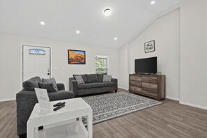 Una sala moderna con un sofá gris, un televisor de pantalla plana sobre un mueble de madera y una alfombra estampada.