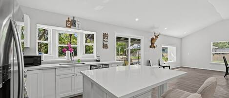 A modern kitchen with white cabinetry, a large island, and a view of the outdoors.